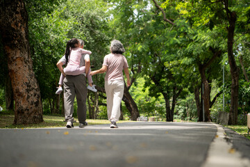 Obraz premium Happy Asian grandparents and granddaughter running joyfully together in a park