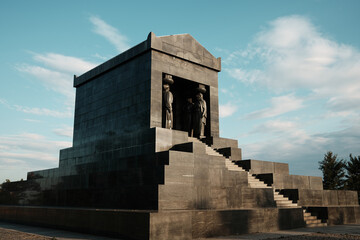 Fototapeta premium Side angle of the Monument to the Unknown Hero in Belgrade, Serbia. Solid granite structure with statues under a bright blue sky at sunset.