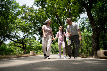 Fototapeta premium Happy Asian grandparents and granddaughter running joyfully together in a park