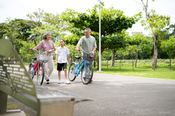 Happy Asian grandparents walking with bicycles alongside their granddaughter in a park