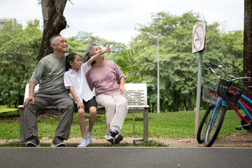 Fototapeta premium Happy Asian grandparents walking with bicycles alongside their granddaughter in a park