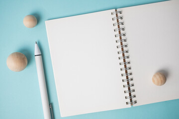 Workspace with empty notebook, pen and wooden ball on blue background.