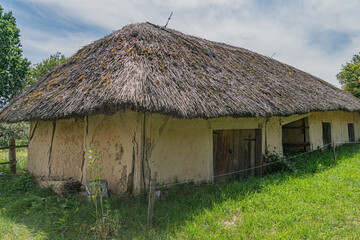 Ancient European rural cottage with thatched roof, likely earth construction cob or similar,...