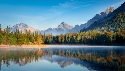 Fototapeta premium a tranquil lake surrounded by dense forests and majestic mountains is mirrored on the surface soft mist covers the area in the early morning light