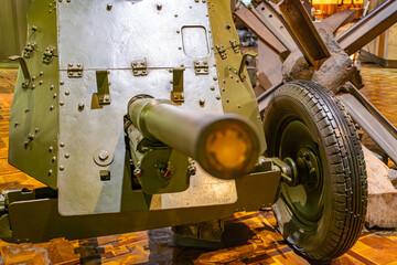 Indoors, large green artillery piece with wheel and round projectile, wooden base, tiled floor, natural light