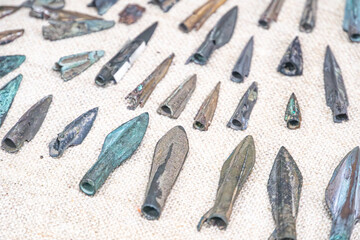 Collection of antique iron arrowheads and tools on a beige fabric, with signs of aging and natural...