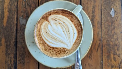 Top down of flat white coffee with latte art in a classic white cup and saucer on rustic wooden table
