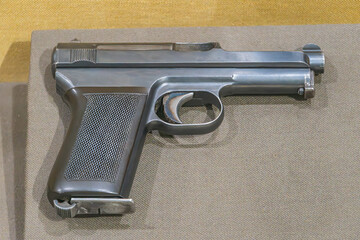 Antique handgun in profile view on table, dark metallic finish, indoor setting with warm lighting