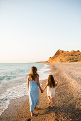 Mother and child daughter holding hands walking at beach over sea outdoors. Summer vacation season. Motherhood.