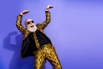 Trendy senior gentleman in gold patterned suit joyfully dancing on purple background showcasing...