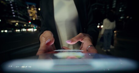 A woman is playing on a mobile phone in the city in the evening. Close-up of a mobile phone in her hands, an unrecognizable person