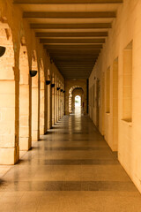 Stone corridor bathed in warm sunlight, featuring arches and columns in golden hues. Balanced symmetry and detailed surfaces highlight classic architectural charm.