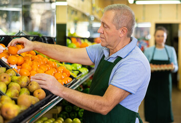 Fototapeta premium in department of vegetables and fruits, man seller chooses ripe and sweet tangerines for buyer