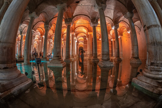 Basilica cistern reflecting on water surface with tourists admiring medusa head in istanbul, turkey