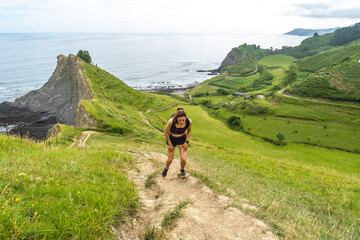 Tired female runner resting on hiking trail in zumaia, basque country, spain