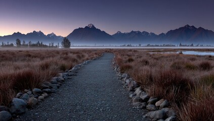 Gravel path leading through a misty landscape toward a mountain range.