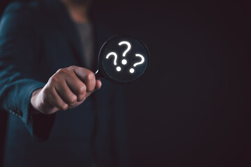 The concept of finding an answer to complex questions in business. Businessman hand holding a magnifying glass with question mark.