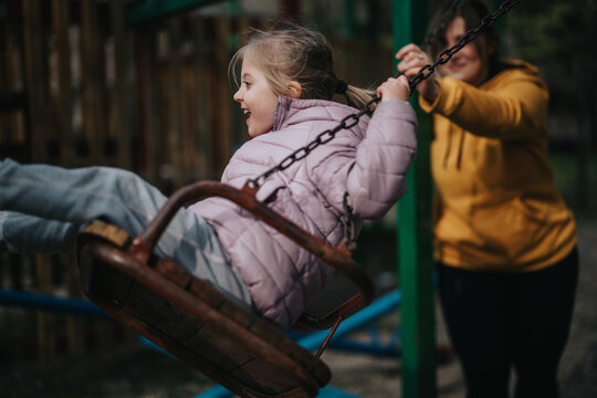 A mother and her young daughter enjoy bonding time as she pushes her on a swing in a park. The cheerful atmosphere shows a joyful connection and the vibrant activity of play. - Powered by Adobe