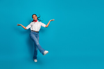 Cheerful young woman posing energetically in casual white shirt and jeans with blue background highlighting joyful lifestyle