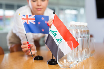 Woman secretary prepares an office for negotiations - she places flags of Iraq and Australia the...