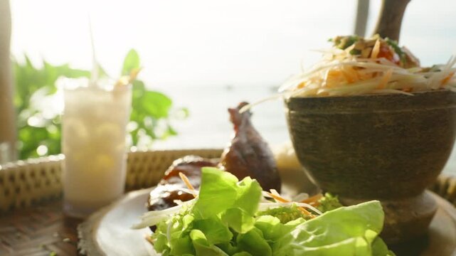 Grilled chicken leg with papaya salad and cold lemonade on rattan tray with sea in background, close up, Traditional Thai Food Concept