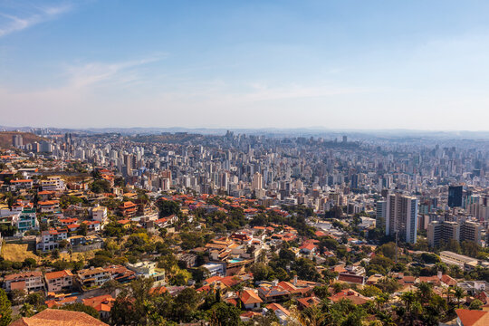 Vista a&eacute;rea de Belo Horizonte, mostrando uma ampla paisagem urbana com pr&eacute;dios altos e bairros residenciais cercados por &aacute;reas verdes, sob c&eacute;u claro
