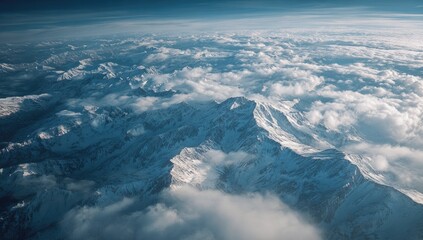 High-altitude view of snow-capped mountains, blanketed by clouds