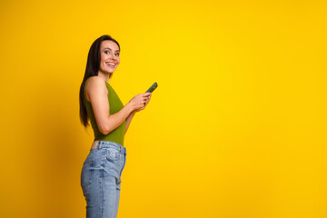 Smiling woman in green tank top holding smartphone against vibrant yellow background