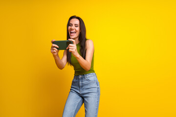 Joyful young woman playing a smartphone game on a bright yellow background, capturing a dynamic and...