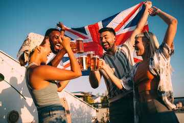 Happy friends toasting with beer and celebrating with uk flag on rooftop