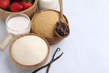 Different ingredients for panna cotta. Milk, sugar, vanilla, chocolate and strawberries on white tiled table, closeup. Space for text