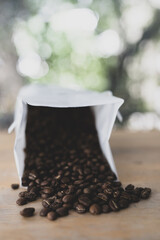 White paper coffee bag packaging on a wooden surface alongside scattered coffee beans