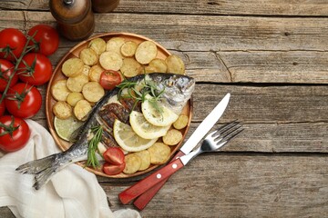 Tasty roasted dorado fish served with potatoes, tomatoes and lemon on wooden table, flat lay and space for text. Homemade seafood dish