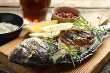 Tasty roasted dorado fish served with rosemary and lemon on wooden table, closeup. Homemade seafood dish