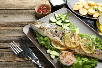 Tasty roasted seabass fish served with vegetables and lemon on wooden table, closeup. Homemade seafood dish