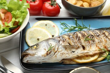 Tasty roasted seabass fish served with salad and potatoes on white wooden table, closeup. Homemade seafood dish