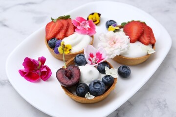 Sweet tartlets with berries and flowers on light marble table, closeup. Delicious dessert