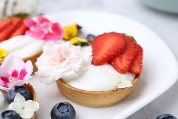Sweet tartlets with berries and flowers on light table, closeup. Delicious dessert