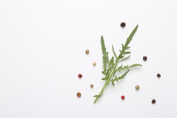 Fresh ripe green arugula leaf and peppercorns on white background, flat lay. Space for text