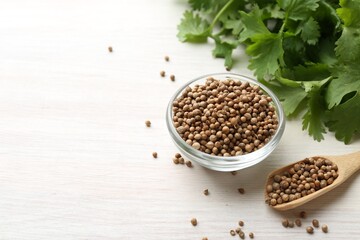 Coriander seeds in bowl, spoon and fresh cilantro leaves on light wooden table, closeup. Space for text