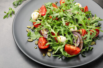 Tasty salad with arugula, mozzarella and vegetables on grey table, closeup