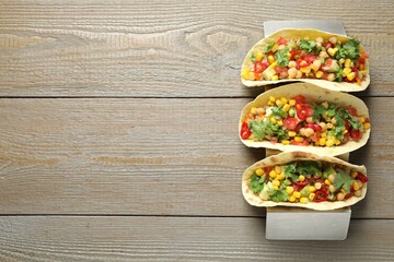 Tasty vegetarian tacos with chickpeas, corn and quinoa served on wooden table, top view. Space for text