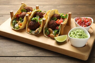 Tasty vegetarian tacos with falafel served with salsa and guacamole on wooden table, closeup