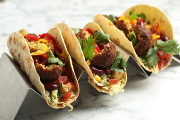 Tasty vegetarian tacos with falafel, tofu, beans and vegetables on white marble table, closeup