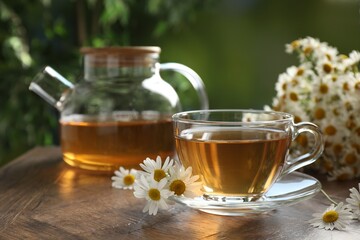 Aromatic tea in glass cup and chamomile flowers on wooden table, closeup