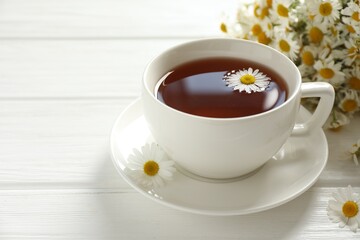 Aromatic tea in cup and chamomile flowers on white wooden table, closeup