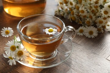 Aromatic tea in glass cup and chamomile flowers on wooden table, closeup