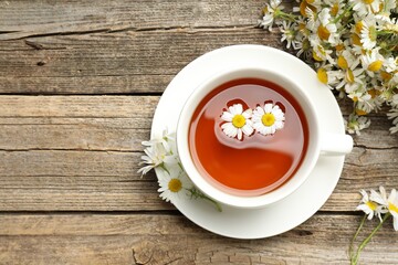 Aromatic tea in cup and chamomile flowers on wooden table, flat lay. Space for text