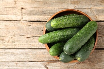 Fresh cucumbers in bowl on wooden table, top view. Space for text