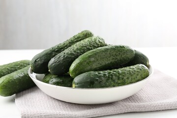 Fresh cucumbers in bowl on white table against grey background, closeup